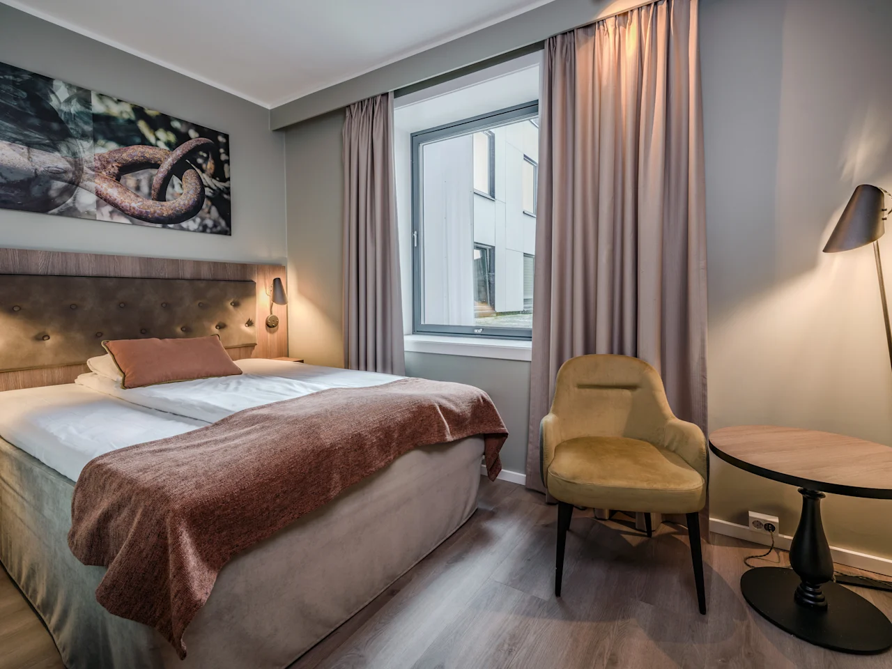 Viihtyisä hotellihuone, jossa on mukava sänky, tyylikäs nojatuoli ja ikkuna, josta avautuu näkymä ulos.