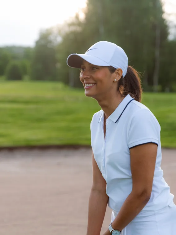 En person i hvit caps og pikétrøye smiler mens de nyter en golfrunde på en solrik dag.