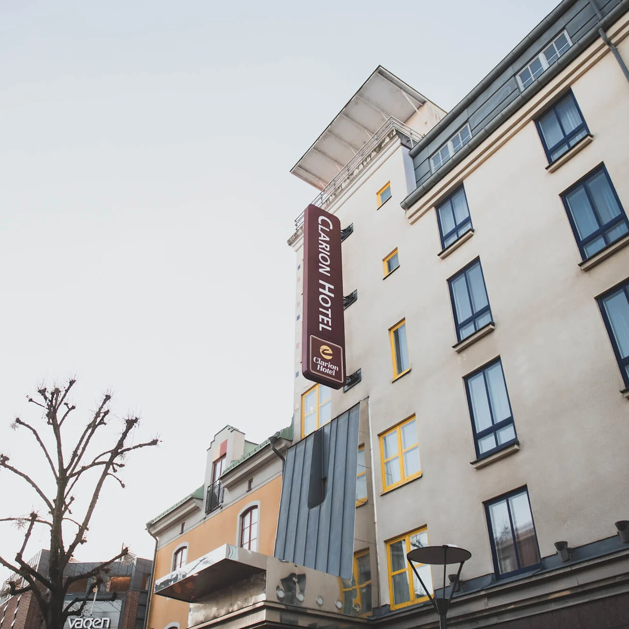 A hotel building with a vertical sign reads "CLARION HOTEL" next to bare trees under a clear sky, creating an urban setting.