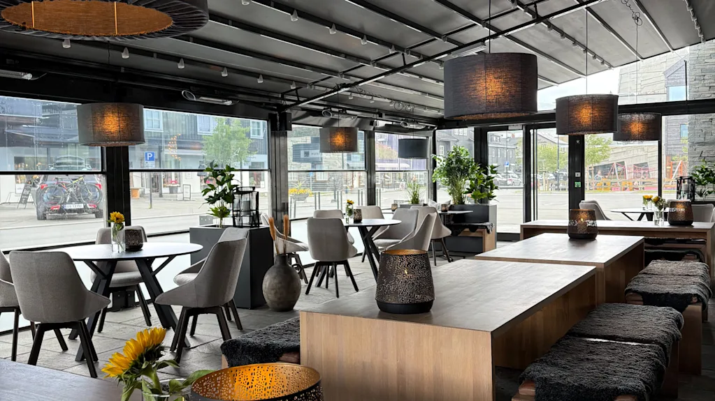 Modern covered outdoor patio with wooden tables, cozy hanging lamps, and decorative lanterns.
