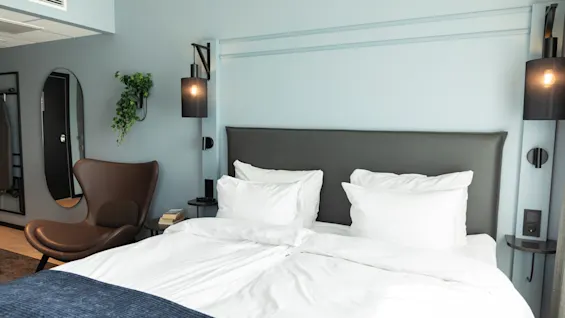 Et koselig hotellrom med en stor seng, en komfortabel lenestol og stilig innredning, med lyseblå vegger og varm belysning.