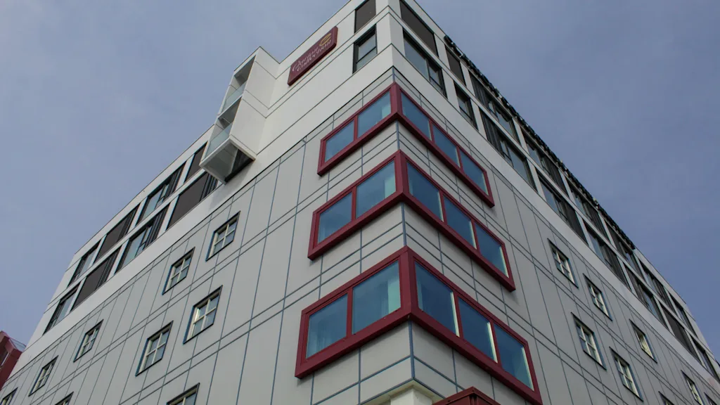 En høj, moderne bygning med rødrammede vinduer strækker sig mod en klar himmel.