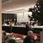 A bar counter with people ordering and drinking, illuminated by hanging lights. The background shows "Quality Hotel Park," and the foreground includes seated patrons at tables.