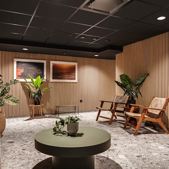 En modern och inbjudande lounge med träribbväggar, bekväma stolar och frodiga gröna växter, vilket skapar en lugn atmosfär.