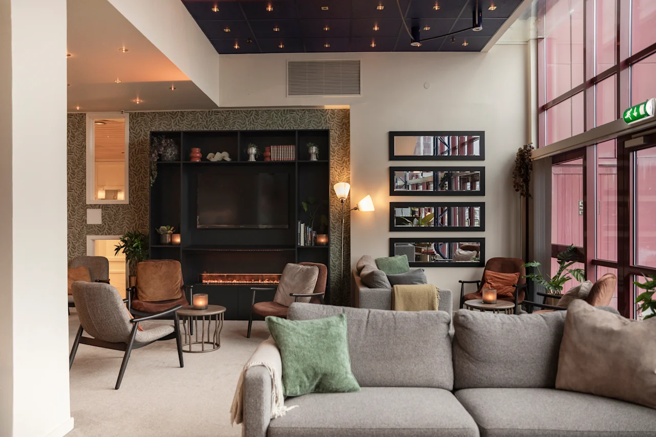 Viihtyisä hotelliaula pehmeällä valaistuksella, muhkeilla sohvilla, takalla ja EXIT-kyltillä korkeiden ikkunoiden lähellä.