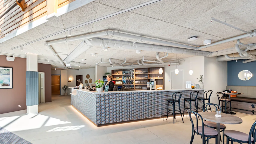 En receptionsområde med disk med mønster og et personalemedlem indenfor et veloplyst moderne interiør med siddepladser og dekorative elementer.