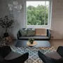A comfortable lounge area with wicker furniture, green cushions, and a view of lush trees through a large window.