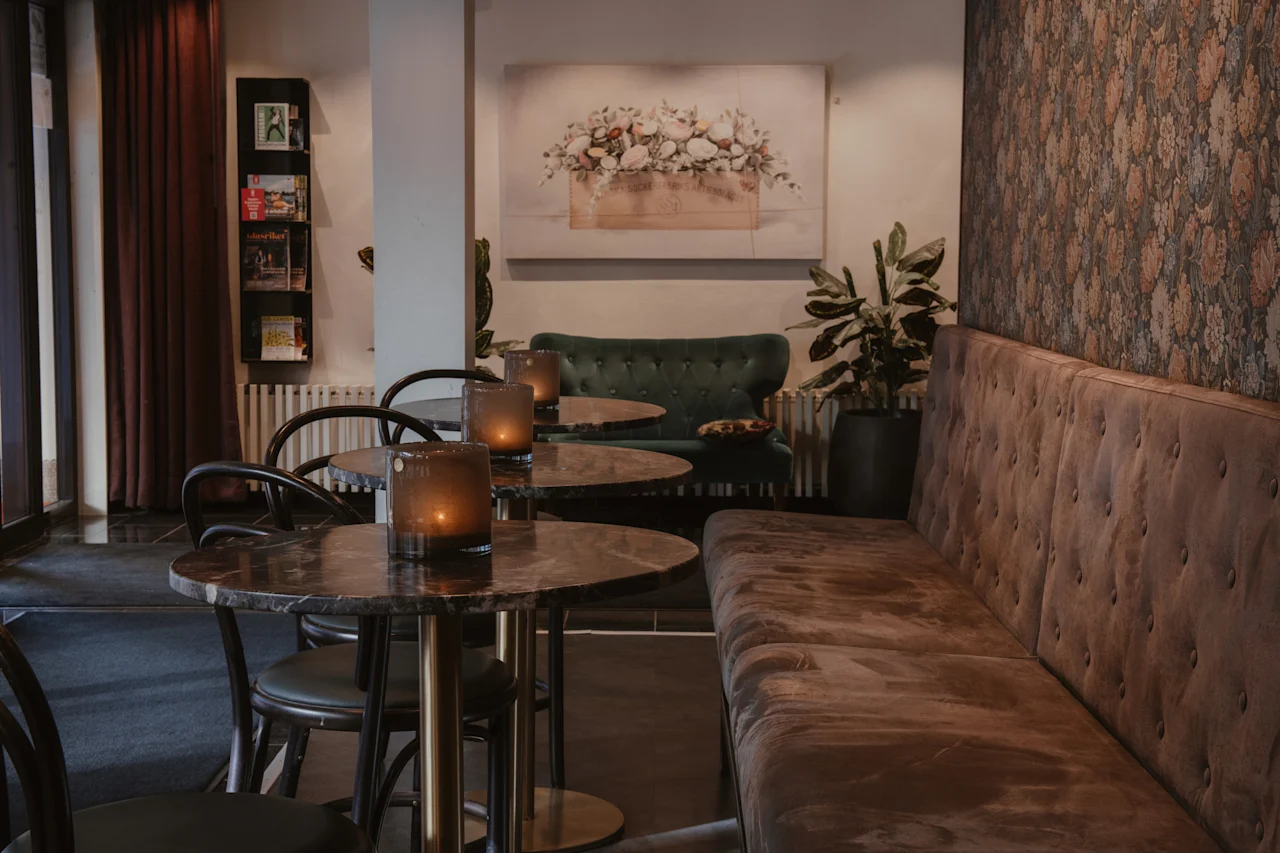 A cozy lounge area with small tables, chairs, and long upholstered benches. Candles glow on the tables, creating a warm ambiance.