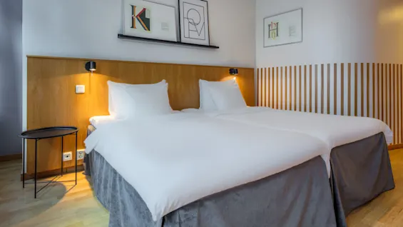Two white beds in a tidy bedroom, with artwork above and a wooden headboard.
