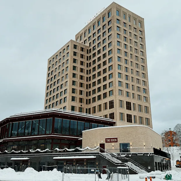 En moderne, høy bygning med en lavere del, med et skilt som leser THE DOCK, omgitt av snø en overskyet vinterdag.