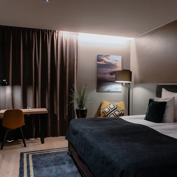 Viihtyisä hotellihuone, jossa on mukava sänky, toimiva työpöytäalue ja lämmin valaistus, luoden rentouttavan tunnelman.