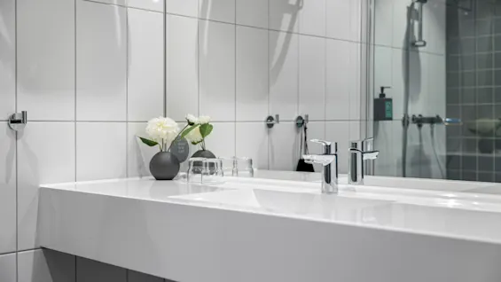 Moderne bad med dobbel vask, kromkraner, hvite flislagte vegger og en dusj som speiles i speilet. Skilt: SAVE THE PLANET.