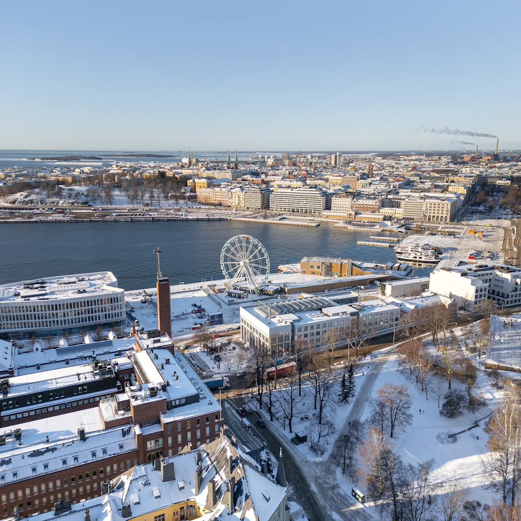 Helsinki from above, a snowy cityscape with a large Ferris wheel by the water under a clear sky.