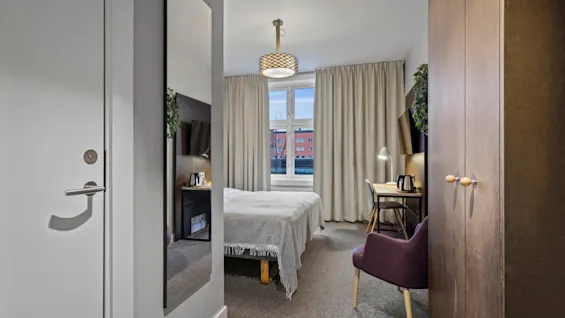 Ett modernt hotellrum med en bekväm säng, en funktionell skrivbordsplats och ett stort fönster med utsikt över staden.