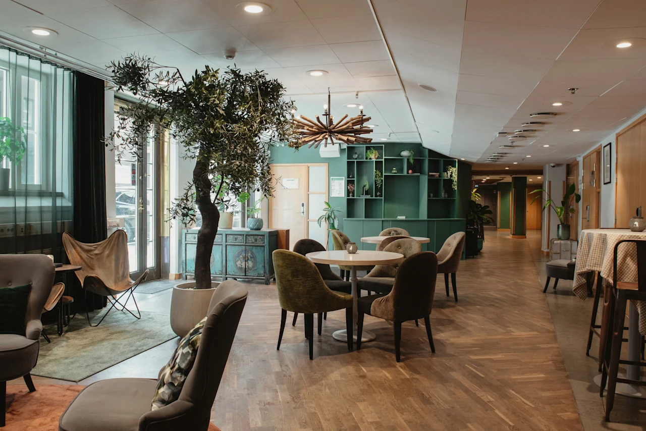 A welcoming hotel lounge with comfortable seating, tables, and a large olive tree, creating a relaxed atmosphere at Home Hotel Uppsala.