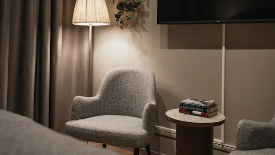 En mysig hörna med en fåtölj, en tänd golvlampa och böcker på ett sidobord, vilket skapar en avkopplande atmosfär.