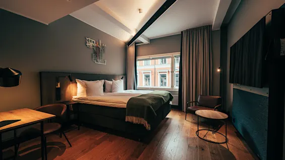 A cozy and modern hotel room with a comfortable bed, a desk, and a large window.