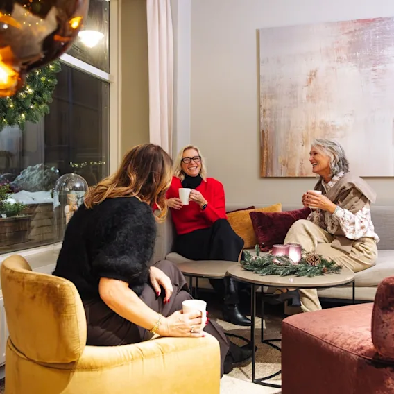 Tre venninner koser seg med varme drikker og en hyggelig samtale i et stilfullt loungeområde på hotellet.