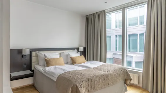 A cozy hotel room with a comfortable bed, warm lighting, and a large window offering a city view. Perfect for relaxation.
