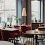 Innbydende restaurantinteriør med røde stoler, trebord og myk belysning. Store vinduer avslører en bygata og TEMPEL HOTEL.