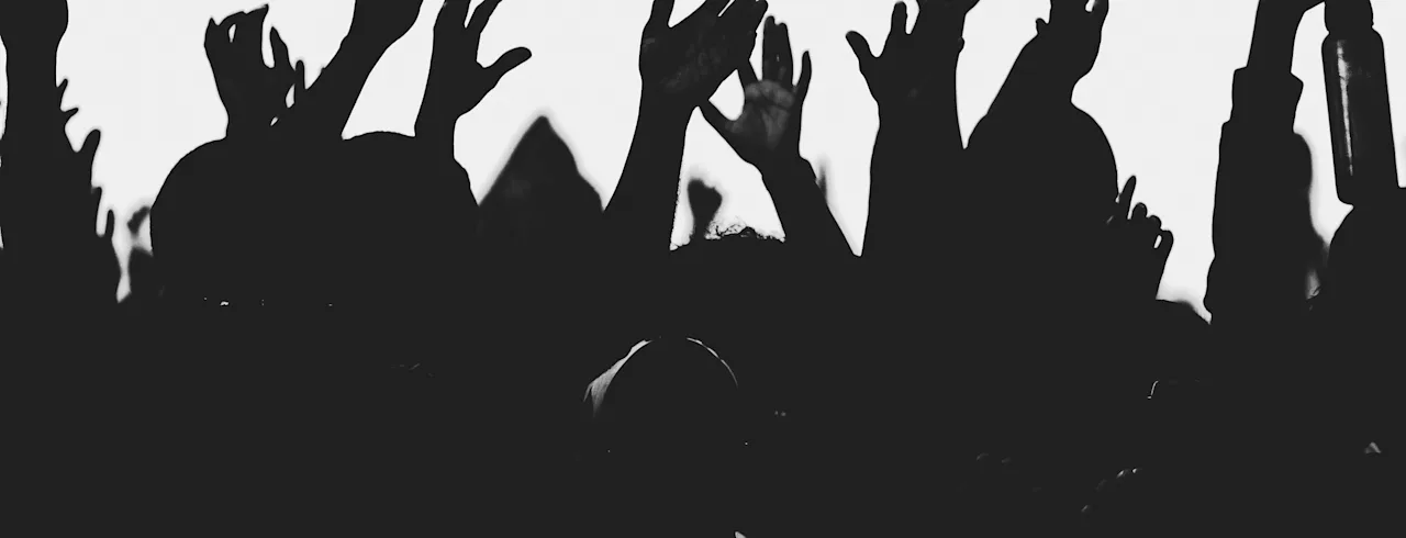 Silhuett av en folkmassa med händerna uppsträckta i luften, som uttrycker entusiasm vid en sammankomst eller evenemang.
