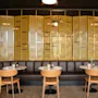 Et koselig restaurantinteriør med en lang brun skinnsofa, små runde bord og en dekorativ gyllen skjerm.