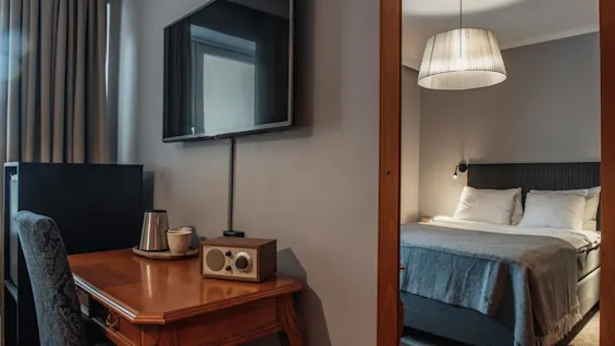 Ett mysigt hotellrum med ett träskrivbord, radio och vattenkokare, en väggmonterad TV och en spegelbild av en bekväm säng.