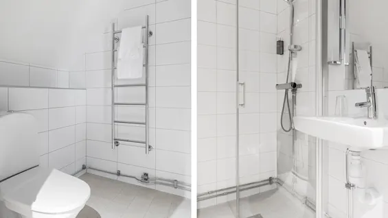 Ett modernt badrum med vita kaklade väggar, inkluderar en toalett och handdukstork till vänster, samt en duschhörna och tvättställ till höger.