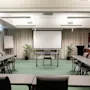 A spacious conference room at Home Hotel Grand Bodø with tables and chairs arranged for a meeting, facing a large projector screen.