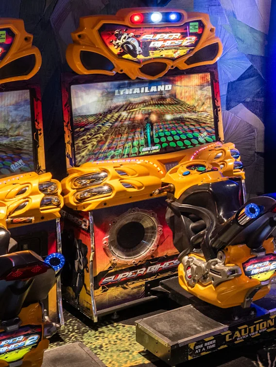 Två färgglada arkadmotorcykelracingspel med skärmar som visar en racerbana, redo för spelare.