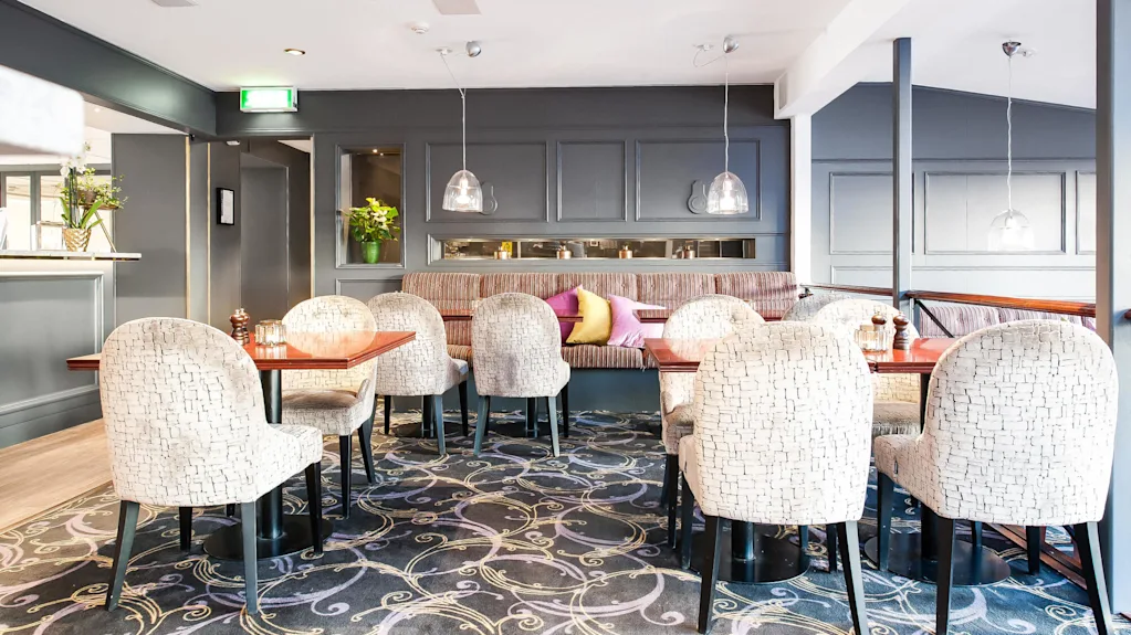An elegantly furnished restaurant with upholstered chairs, decorative lighting, and a plush carpet in an inviting space without patrons.