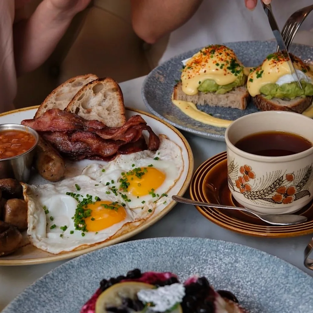 Venner nyder en solid morgenmad med et udvalg af retter, herunder spejlæg, bacon, avocadotoast og søde pandekager.
