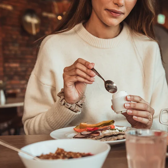 En kvinna äter ett kokt ägg till frukost i en mysig restaurangmiljö.