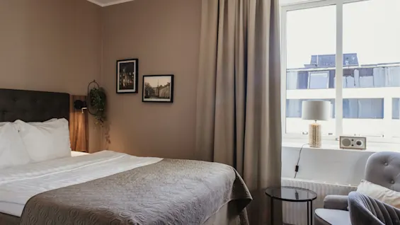 Viihtyisä hotellihuone, jossa on mukava sänky, suuri ikkuna ja oleskelutila, täydellinen rentoutumiseen.