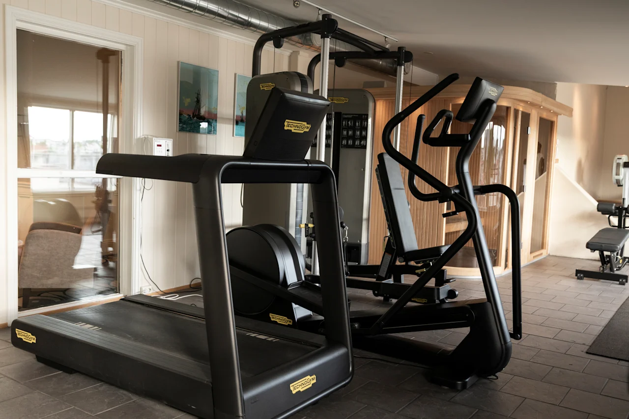 Et lyst og indbydende fitnessområde med moderne træningsudstyr og en træsauna, perfekt til en forfriskende træning.