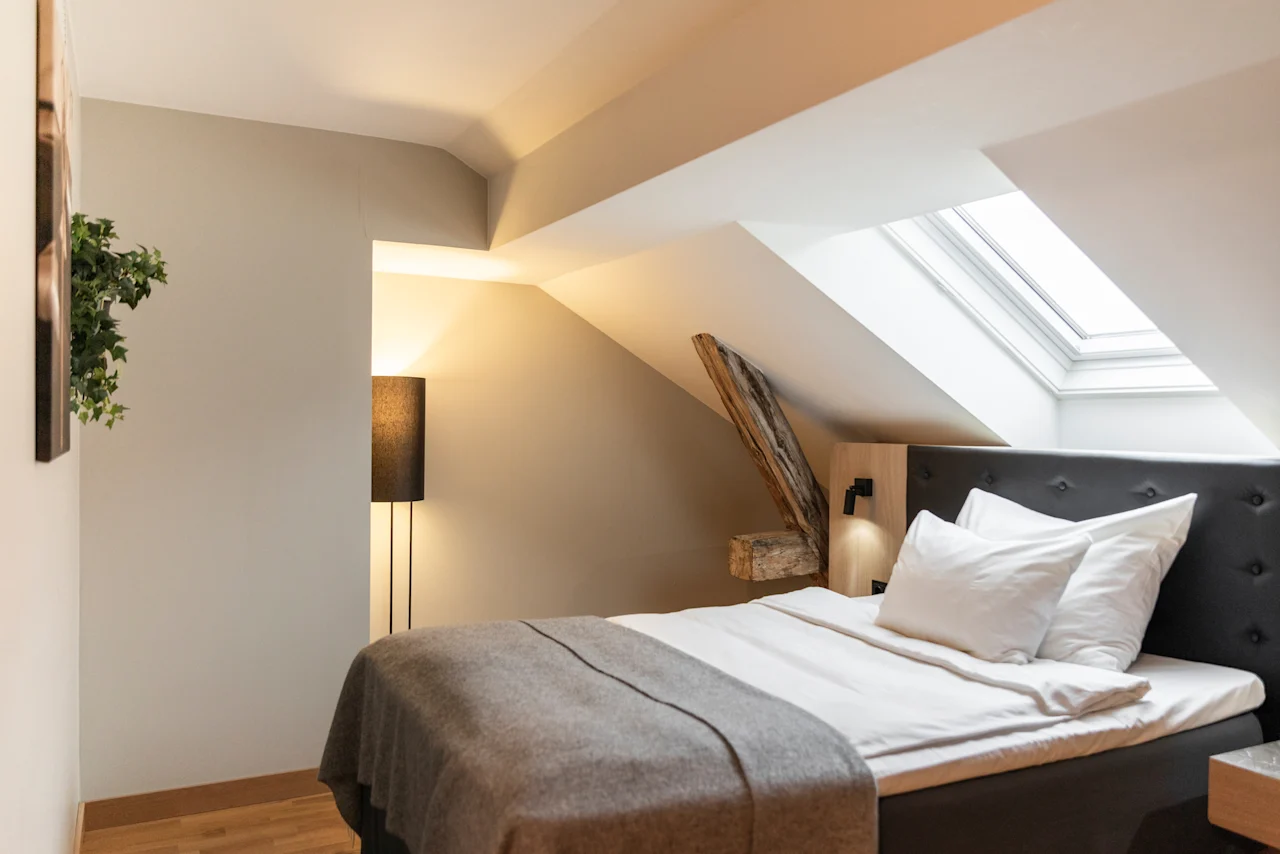 A cozy bedroom with a bed, a floor lamp, and a skylight in a room with sloped ceilings.