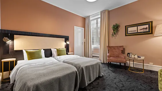 Et koselig hotellrom på Home Hotel Gabelshus med to senger, en komfortabel stol og et vindu med naturlig lys.