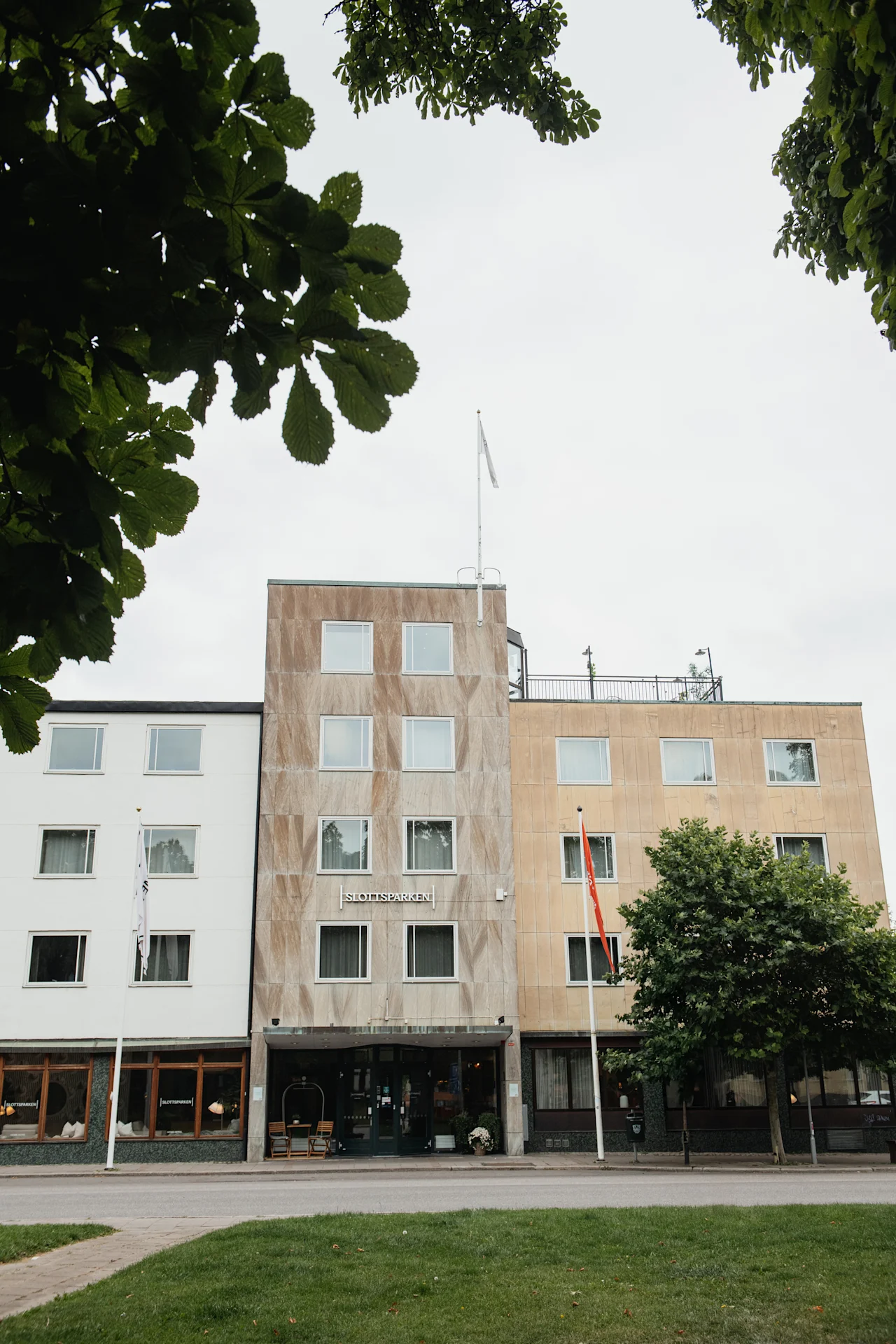 A multi-story building with the text SLOTTS PARKEN on its facade, framed by green trees under a cloudy sky.