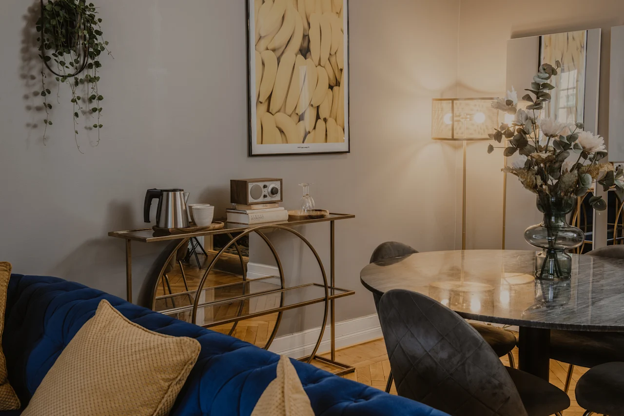 En elegant och bekväm hotellvardagsrumsdel med en blå soffa, ett matbord och en gyllene konsol, vilket skapar en välkomnande atmosfär.