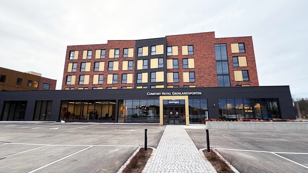 Moderne hotellbygning med stor parkeringsplass og gangvei. Tekst på bygget: Hotel Grenlandsporten. 