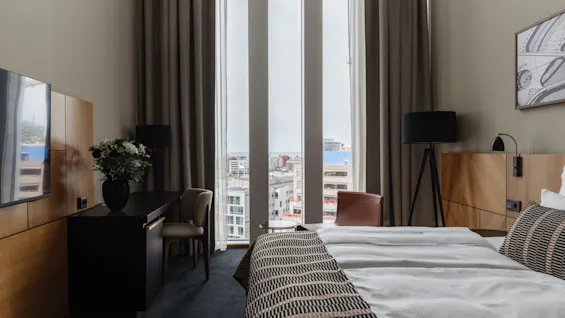 Et moderne hotellrom med et stort vindu som tilbyr byutsikt, med en komfortabel seng og en funksjonell arbeidsplass.