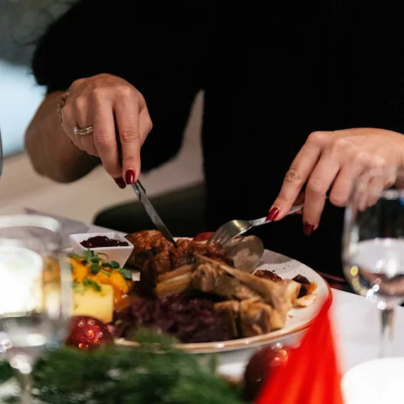 En persons hender skjærer i et deilig måltid med kjøtt og tilbehør ved en festlig borddekking.