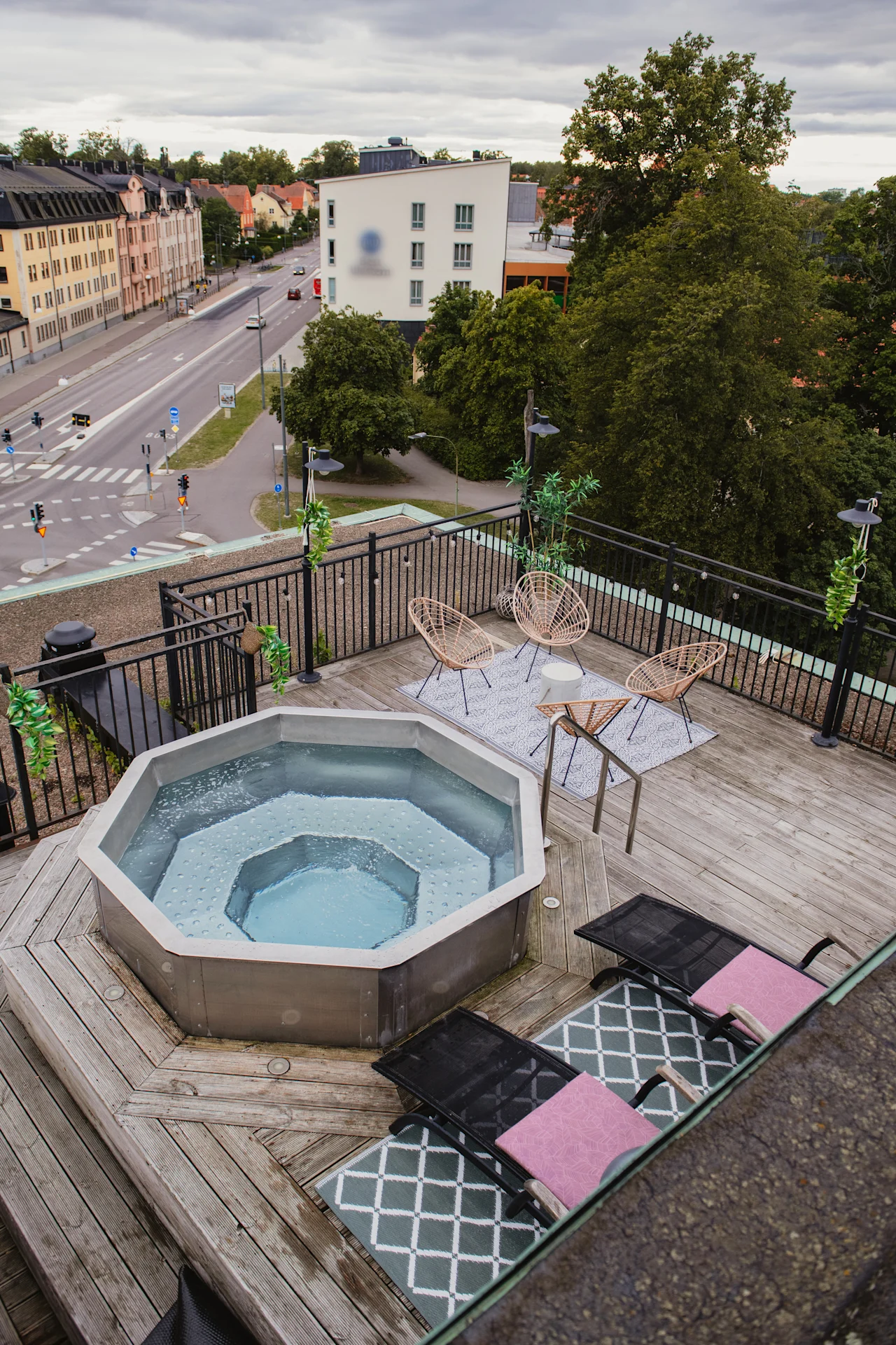 Rooftop terrace with a bubbling hot tub, lounge chairs, and wicker seating, offering a view of the city below.