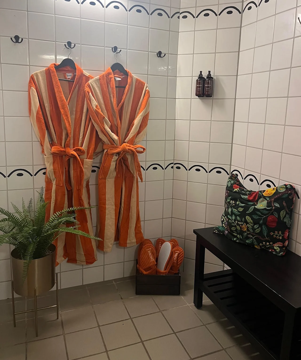 Et koselig velværeområde med to stripete badekåper, tøfler og en plante. En blomstret veske hviler på en benk. Home Hotel Bilan Wellness.