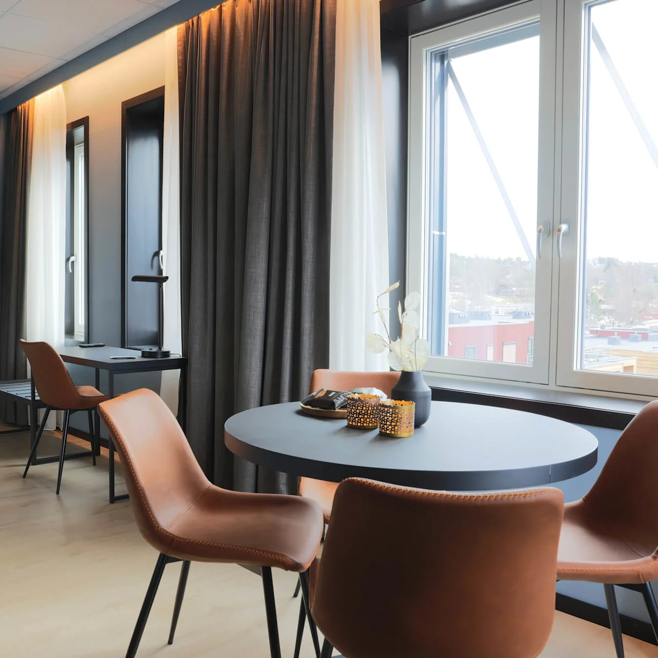 A contemporary room with a round table, leather chairs, curtains, and a view of the exterior.