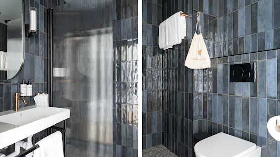 Et moderne badeværelse på Hernö Gin Hotel med mørkeblå fliser, en riflet glasbruser og en håndvask. En pose med teksten et bæredygtigt valg er synlig.