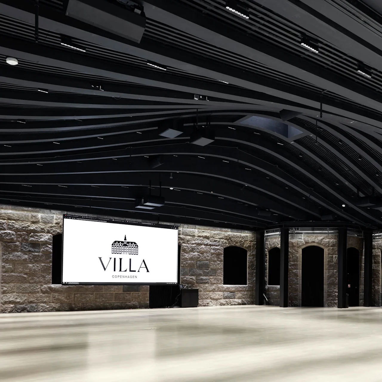 A large room features a modern, undulating ceiling with lights. The stone walls have arched windows. "Villa Copenhagen" text is displayed on a screen at the front.