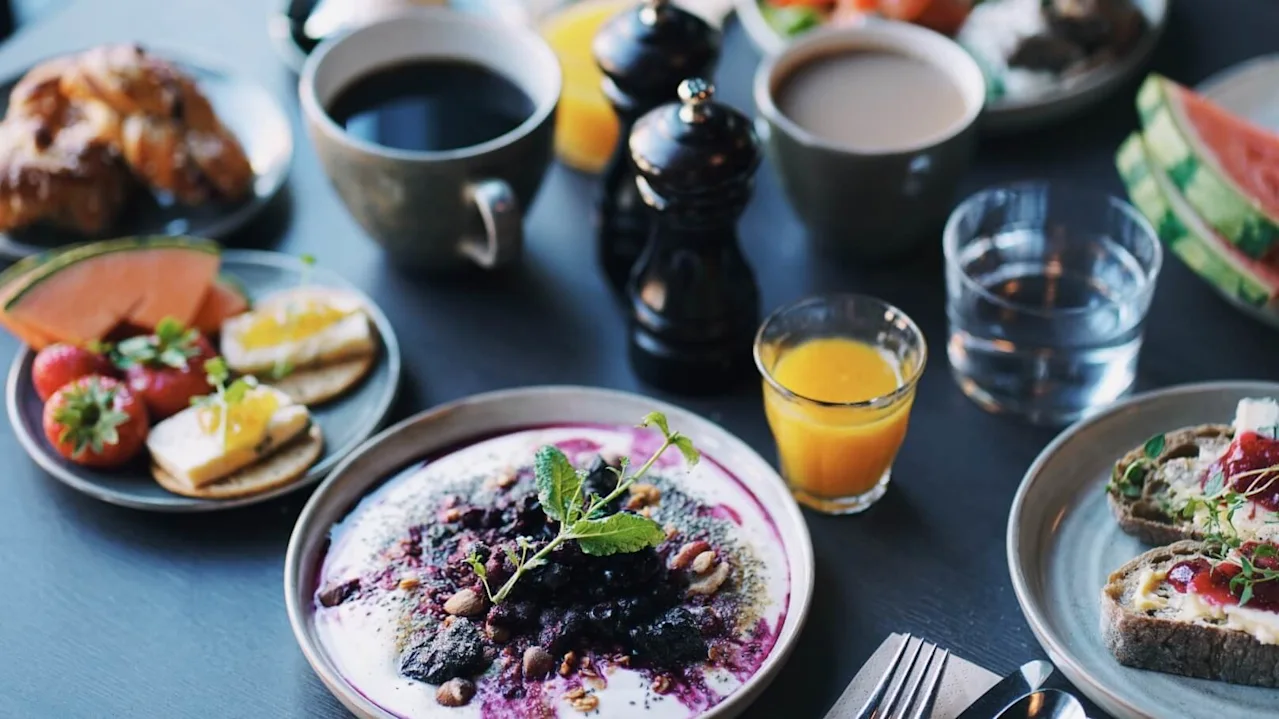En variation av frukostmat utspridd över ett bord med bakverk, frukt och kaffe. Miljön är avslappnad med fokus på måltiden.