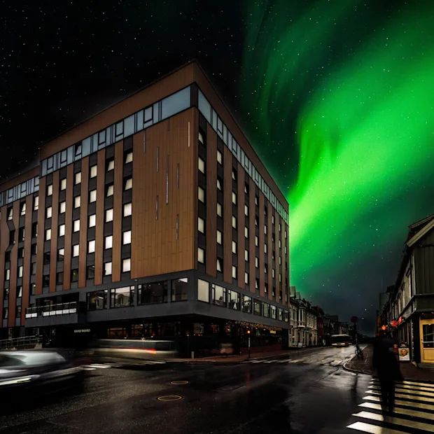 Yökuva rakennuksesta nimeltä THE EDGE eloisan revontulen alla, katu valojuovineen ja kävelevä henkilö. 