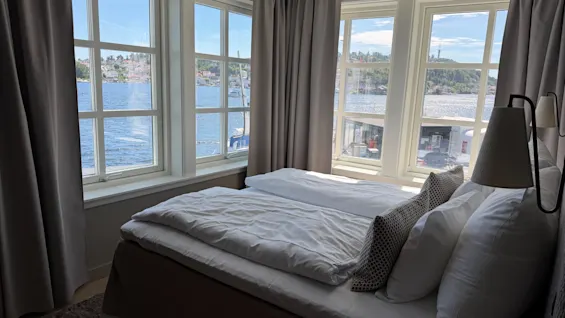 A cozy bedroom with a bed and large windows offering a beautiful view of a calm body of water and distant land.